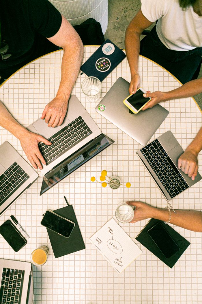 why-choose-us-02 Top view of a team collaborating with laptops, phones, and notes in a modern office.